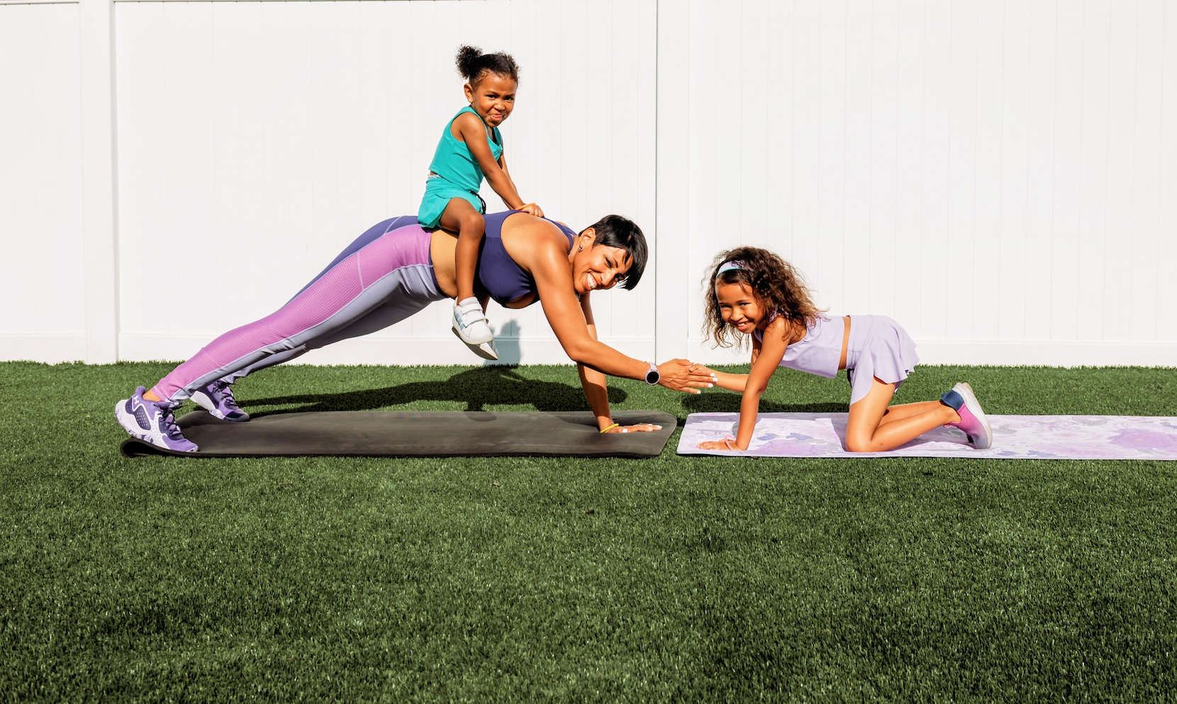 A parent exercising outdoors with two children during a family fitness session